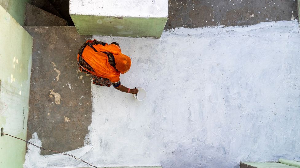 A woman paints the roof of her home with white paint (Credit: Mitul Kajaria)