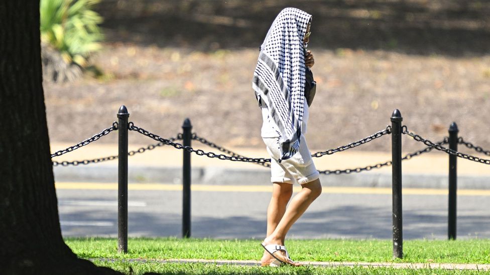 A pedestrian covers their head with scarf while walking in sunshine (Credit: Getty Images)