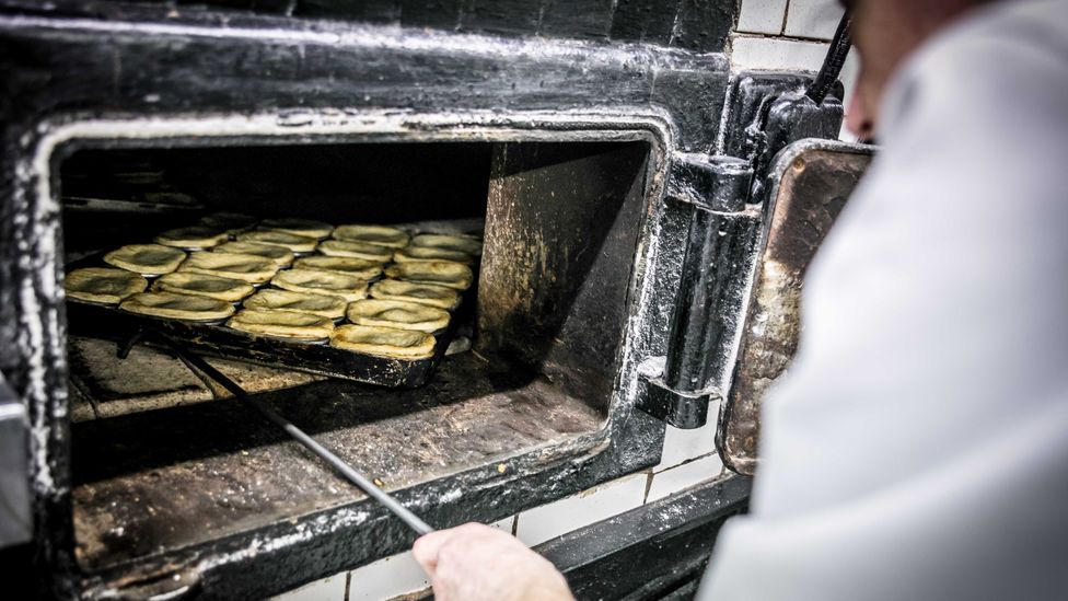 Baker pulling a tray of eel pies of out an oven